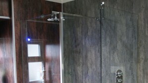 Un baño moderno con cabina de ducha de vidrio, estanterías de madera y pared de mármol.