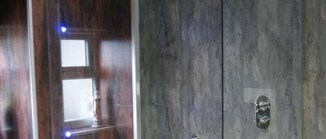 A modern bathroom with a glass-enclosed shower, wooden shelving, and a marble wall.