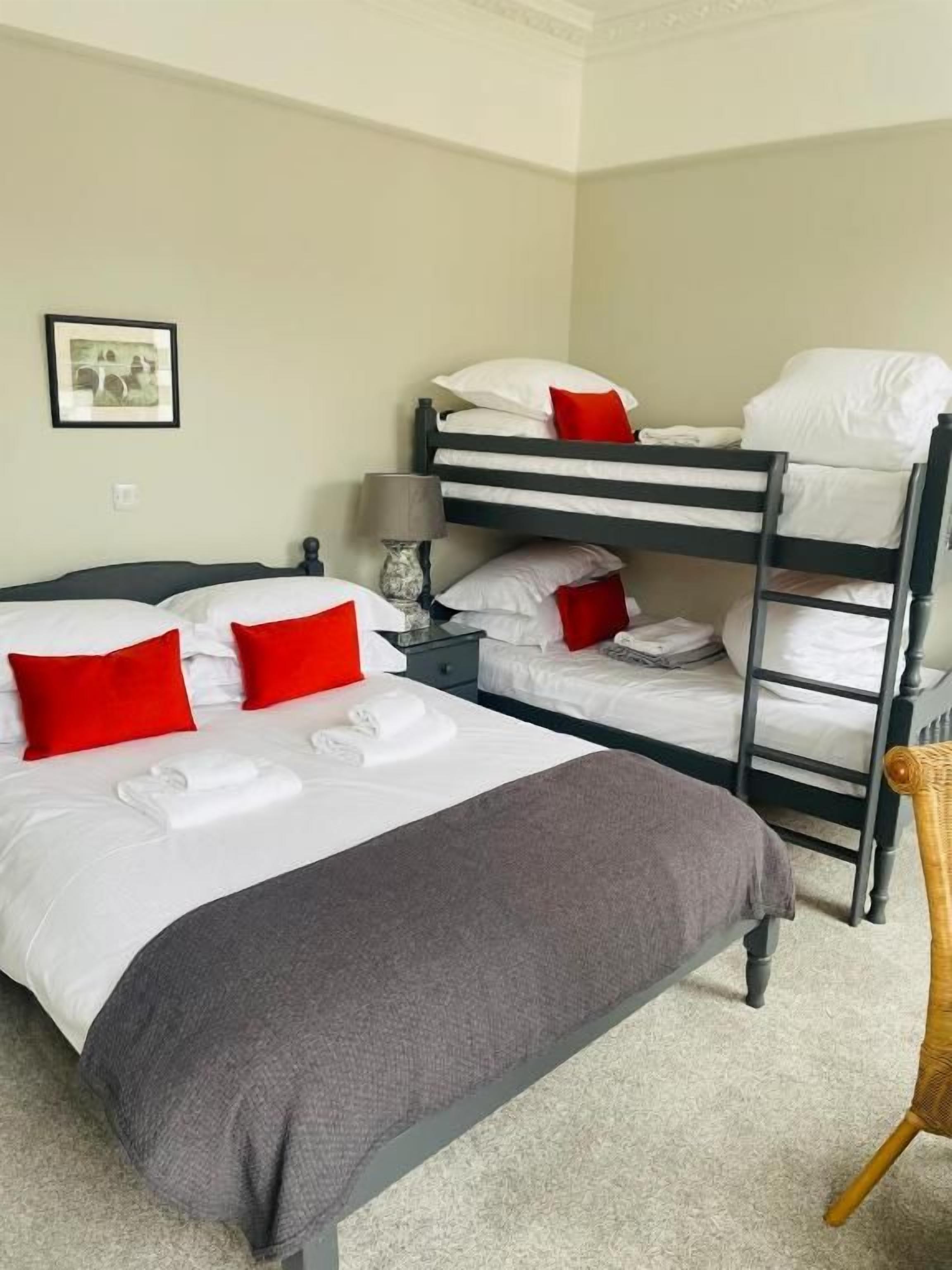 Een hotelkamer met stapelbedden, een enkele bed, een stoel en een lijst met een ingelijst plaatje aan de muur.