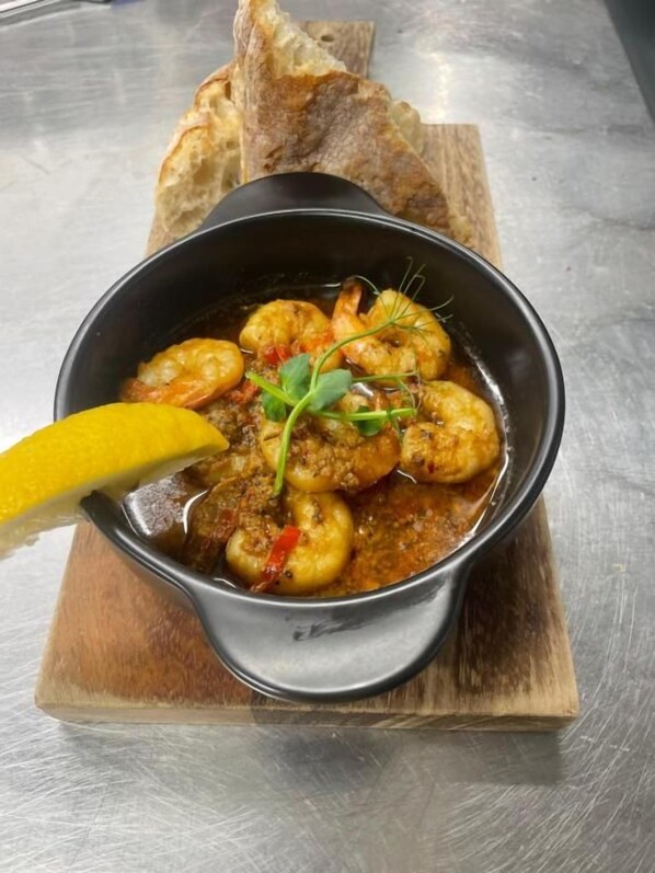Un plato de estofado de camarones con una cuña de limón y pan sobre una tabla de madera.