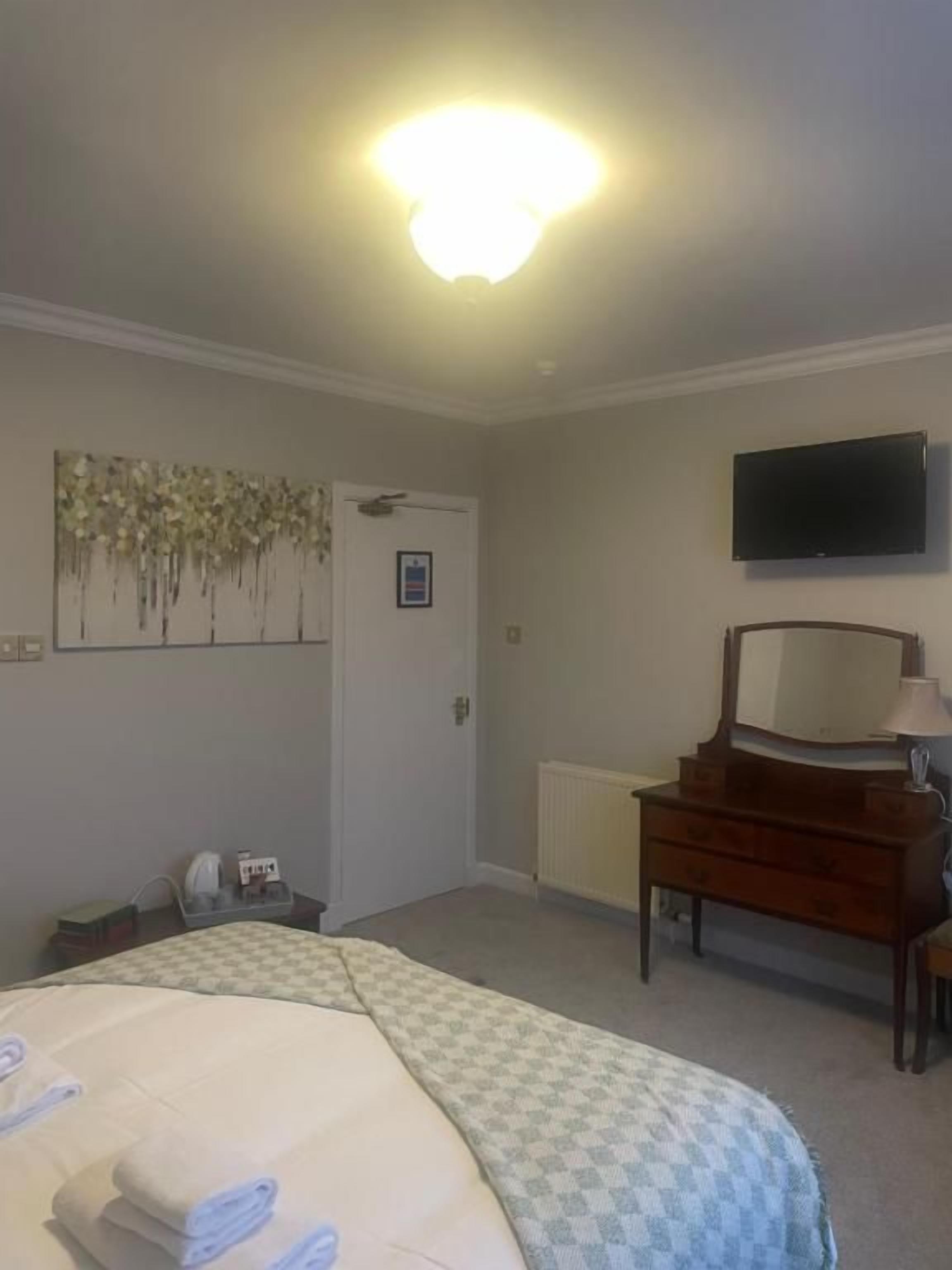 A hotel room with a bed, a dresser, a television, and a painting on the wall.