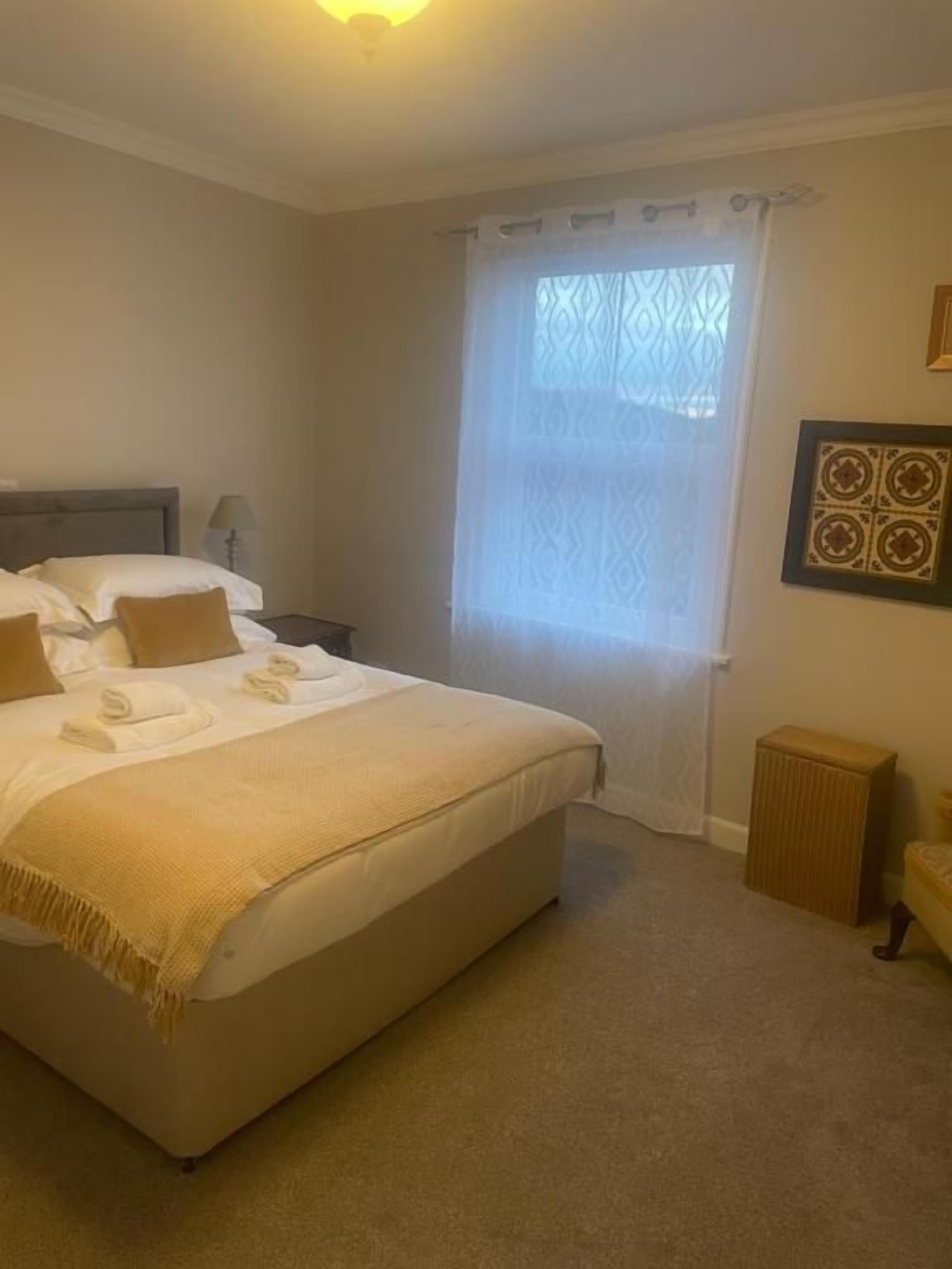 Un dormitorio con cama, mesita de noche, lámpara, radiador y ventana con cortinas.