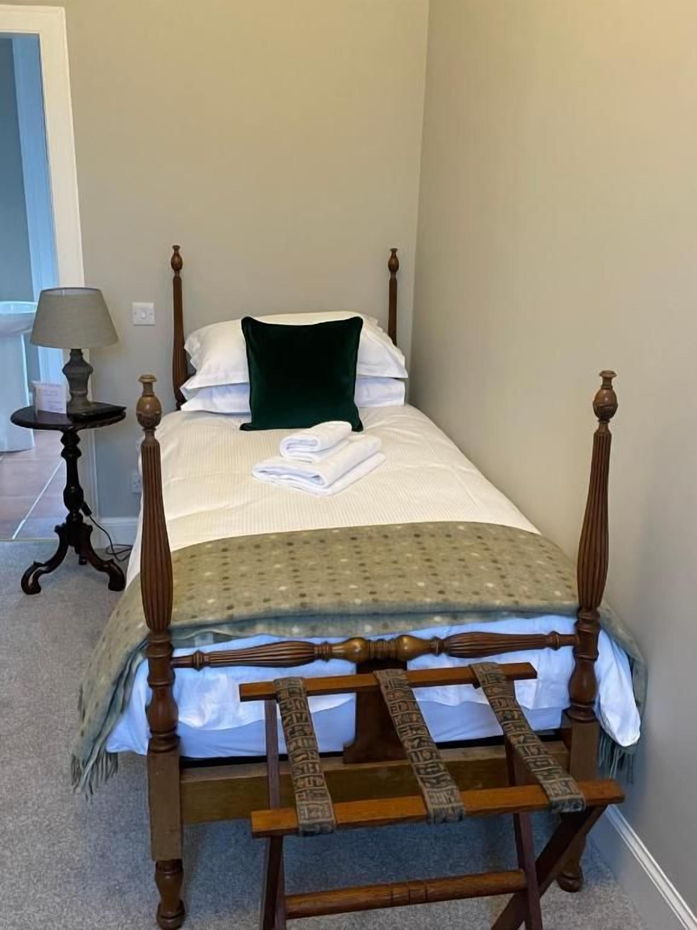 A single bed with a wooden frame, a green pillow, and a white blanket.