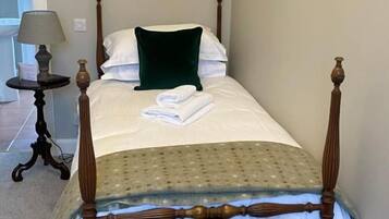 A single bed with a wooden frame, a green pillow, and a white blanket.