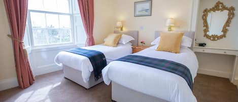 A hotel room with two beds, a window with curtains, a framed picture on the wall, and a mirror above the bed.