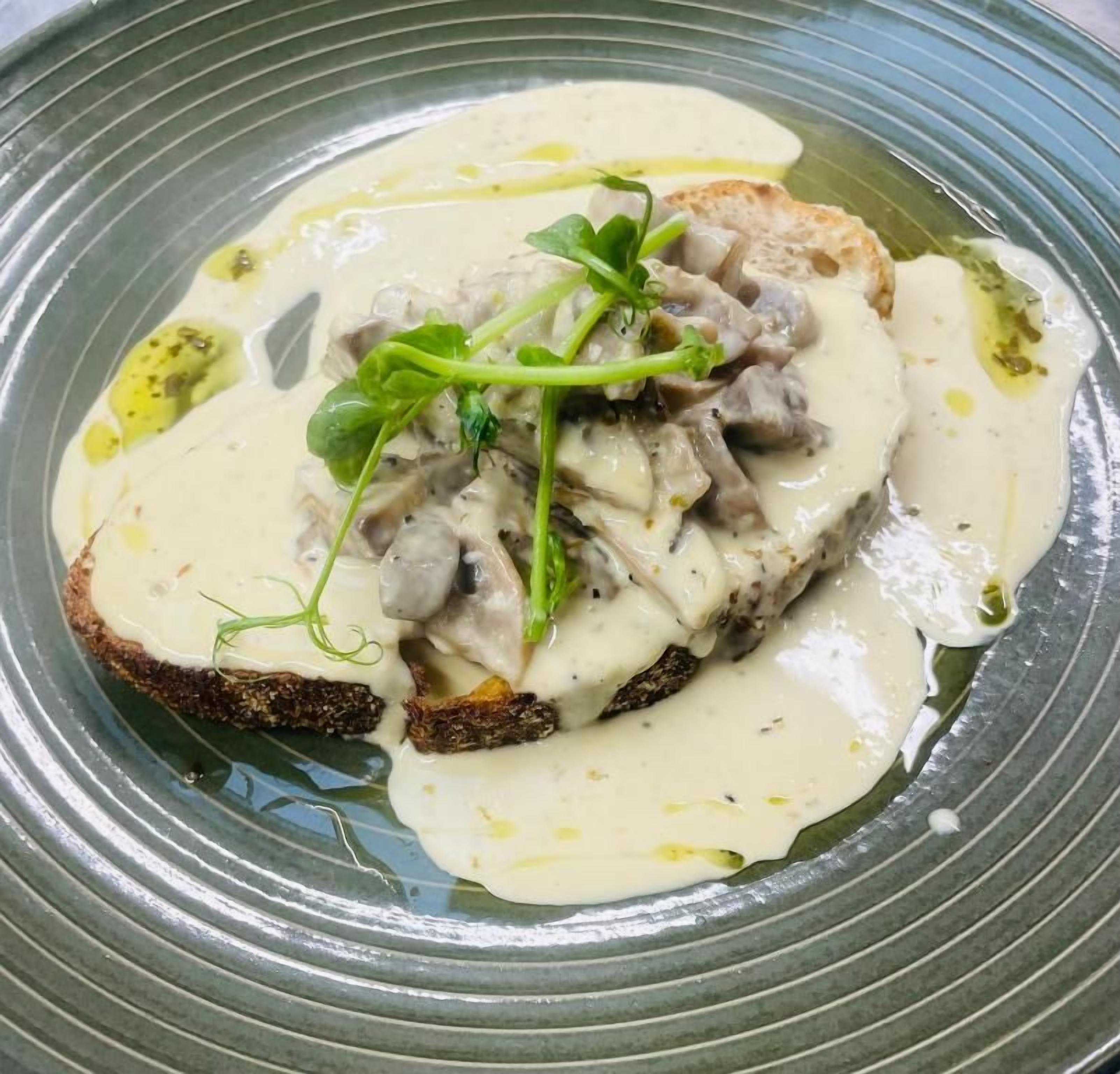 A plate with a creamy mushroom topping, greens, and a slice of bread.