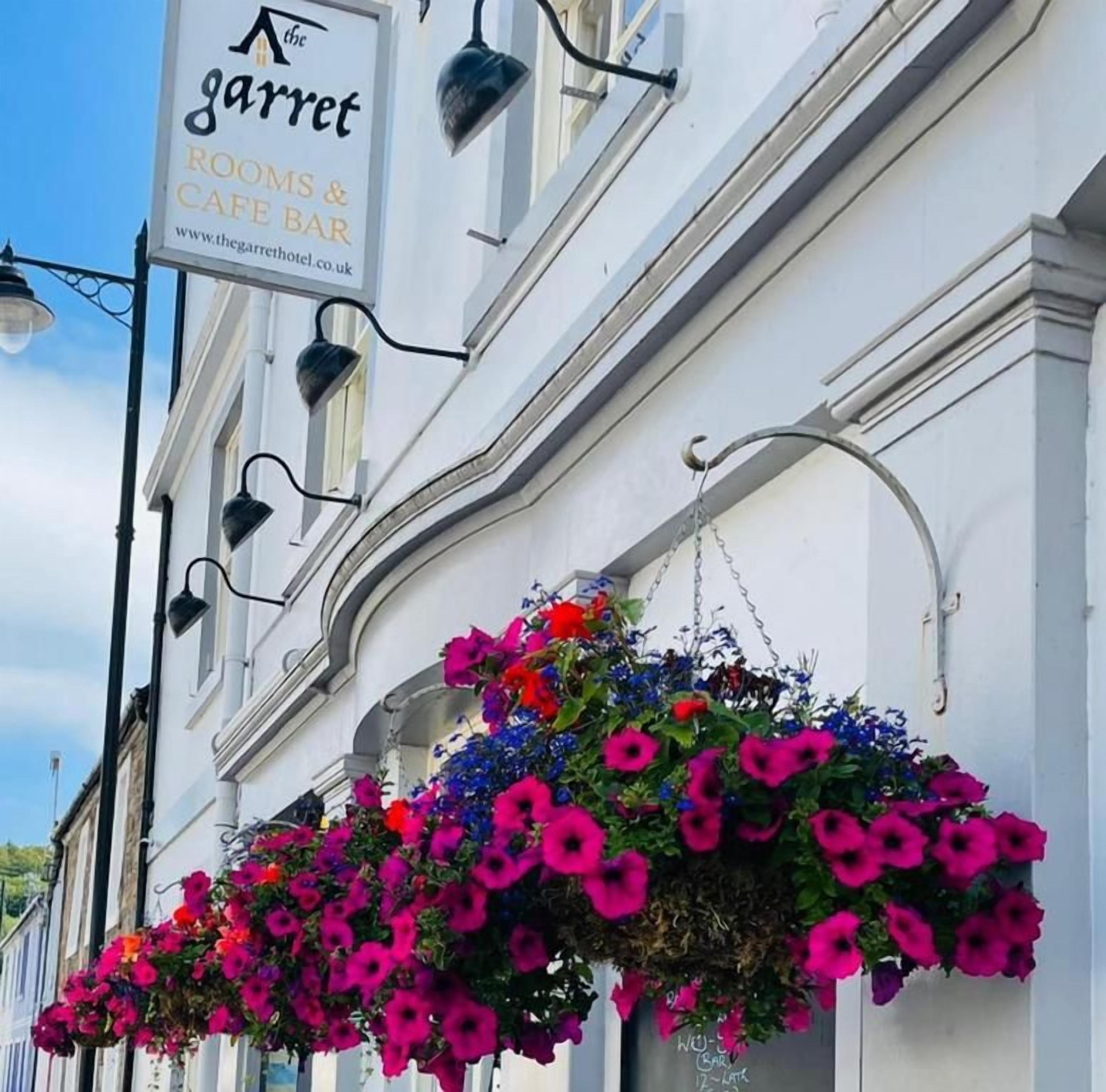 Um edifício com a placa 'The Garret Rooms & Cafe Bar' e cestos de flores pendurados.