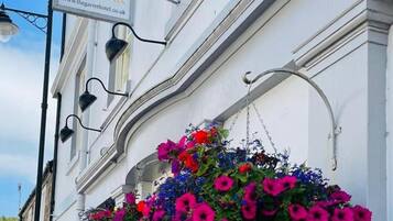 Um edifício com a placa 'The Garret Rooms & Cafe Bar' e cestos de flores pendurados.