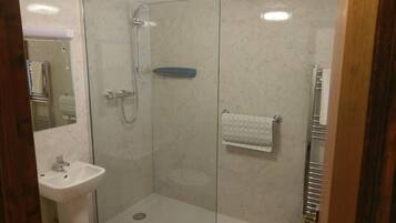 Une douche fermée par des parois en verre, dotée d’un pommeau de douche à main, d’un lavabo blanc et d’un porte-serviettes.