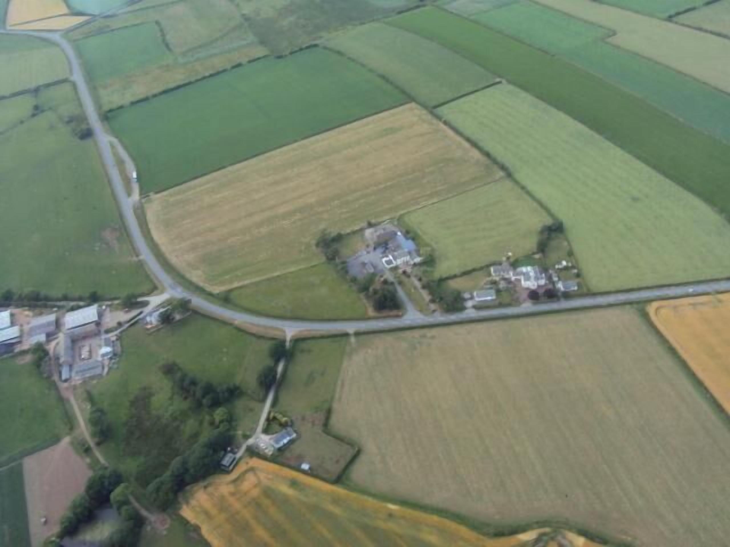 Vista aérea de una zona rural con campos, una carretera y un pequeño conjunto de edificios.