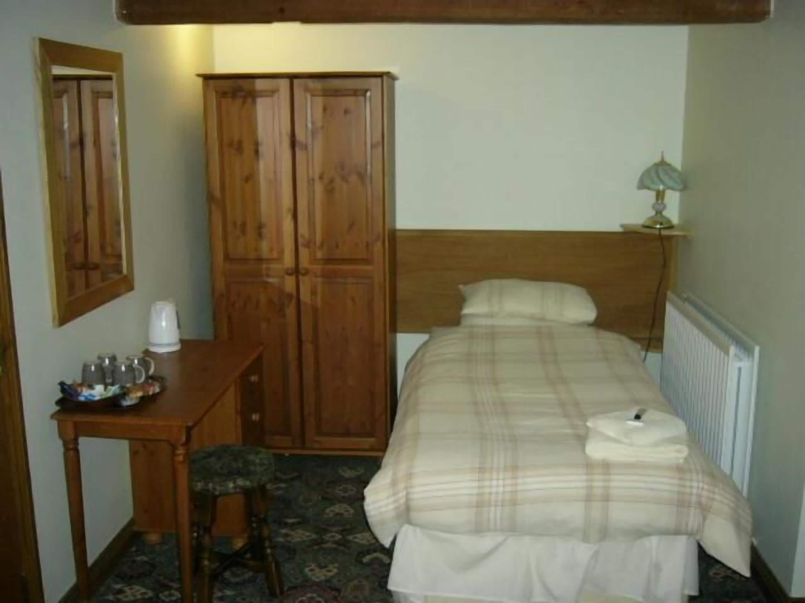 Un dormitorio con una cama, un armario de madera, una mesita con una tetera y una lámpara.