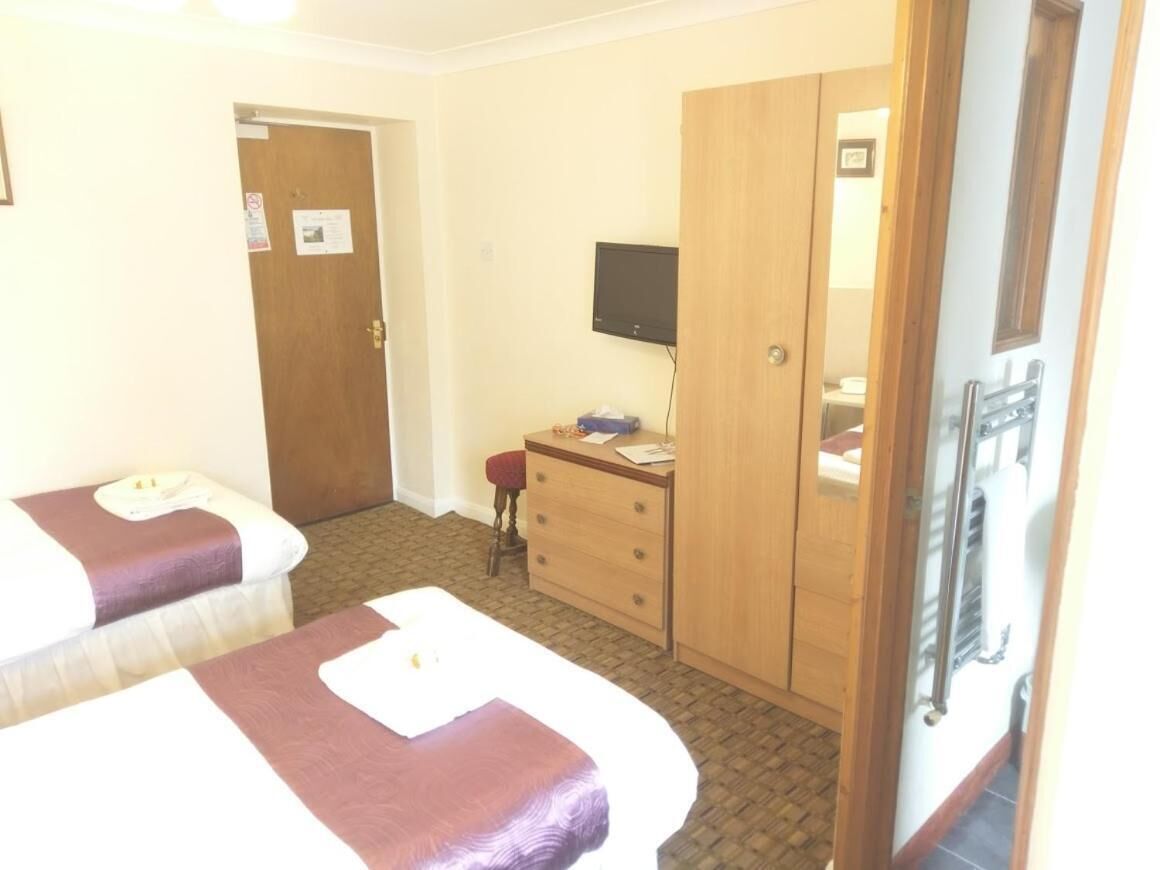 A hotel room with two beds, a wooden wardrobe, a desk with a chair, and a television.