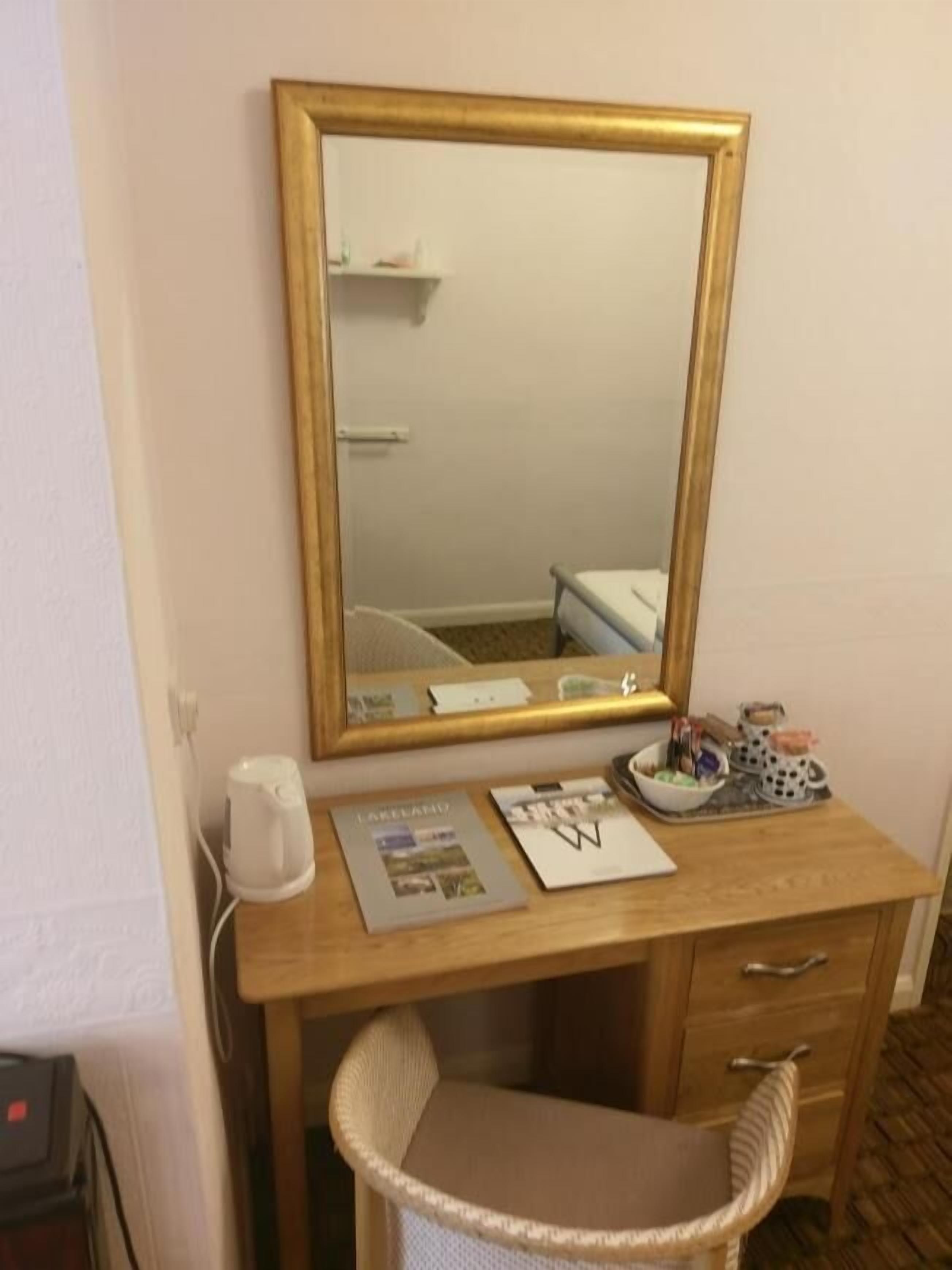 Un escritorio de madera con un espejo, una silla de mimbre y una mesita con un cuenco y una taza.