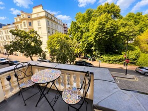 A balcony with a table and chairs, overlooking a street with cars and buildings. - Jubilee Hotel Victoria (London)