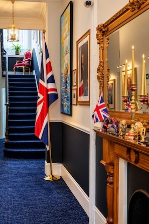 A staircase with blue carpeting, a red and white flag, and a wooden mantelpiece with a mirror and candles. - Jubilee Hotel Victoria (London)