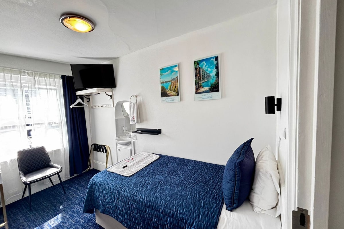 A hotel room with a bed, a chair, a sink, a mirror, a television, and two framed pictures on the wall.