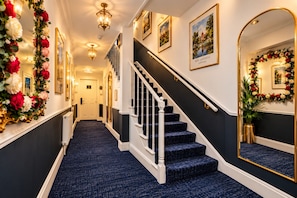 A hallway with a staircase, framed pictures, and floral decorations. - Jubilee Hotel Victoria (London)