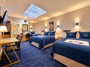 A hotel room with two beds, a desk, a chair, a mirror, a TV, and a skylight. - Jubilee Hotel Victoria (London)