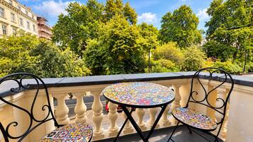 A balcony with two round tables and chairs, a balustrade, and a view of trees and buildings.