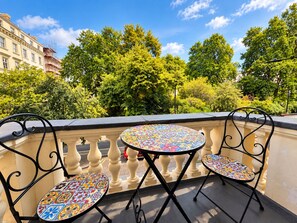 A balcony with two round tables and chairs, a balustrade, and a view of trees and buildings. - Jubilee Hotel Victoria (London)