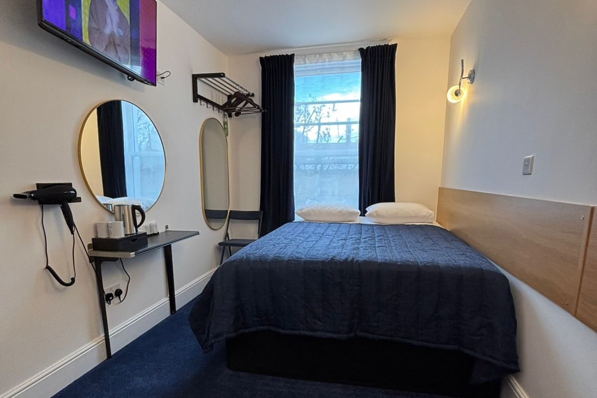 A hotel room with a bed, a mirror, a TV, a hairdryer, and a window with curtains.