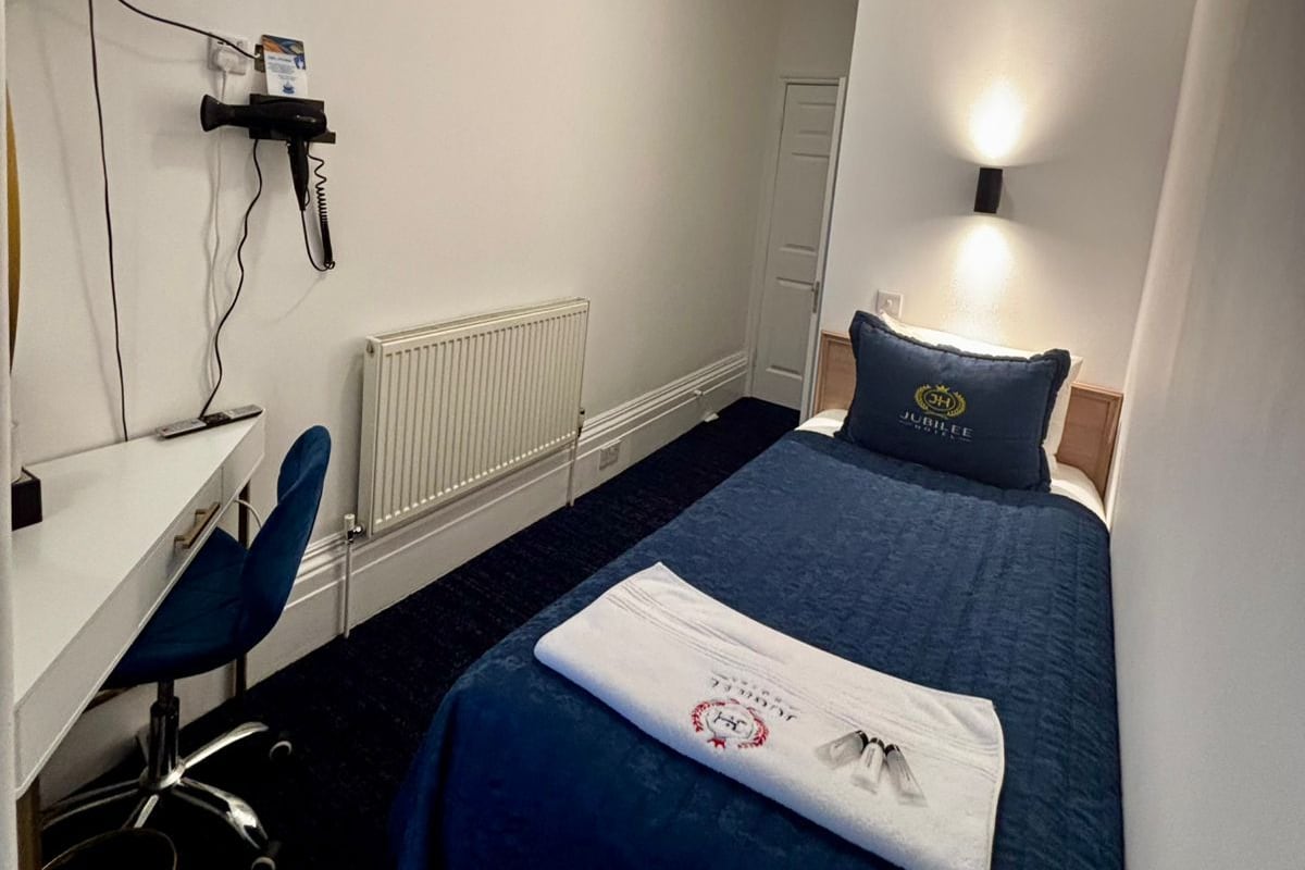 A hotel room with a bed, a desk, a chair, a television, and a radiator.