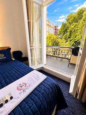 A hotel room with a bed, a window, and a view of a balcony with outdoor furniture. - Jubilee Hotel Victoria (London)