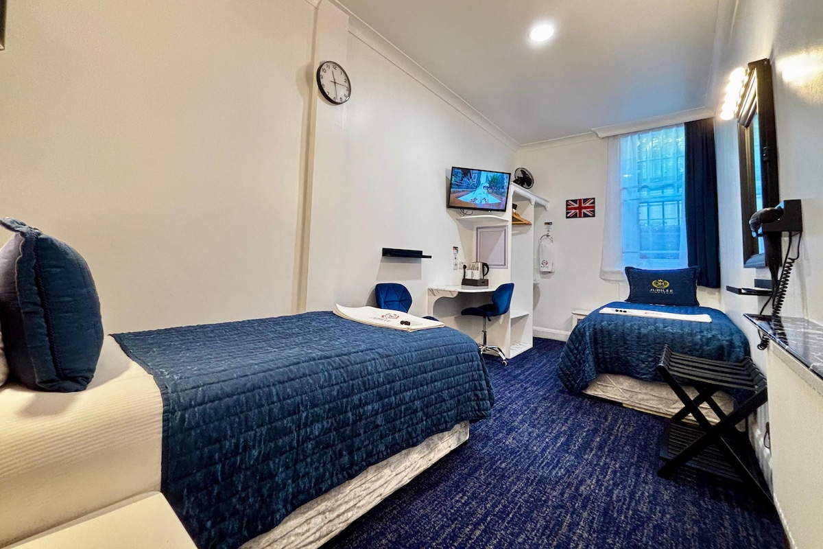 A hotel room with two beds, a desk, a TV, a clock, and a window with a view.