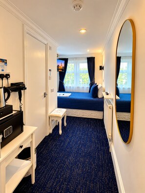 Una habitación de hotel con una cama, un escritorio con computadora, un espejo y una ventana con cortinas.