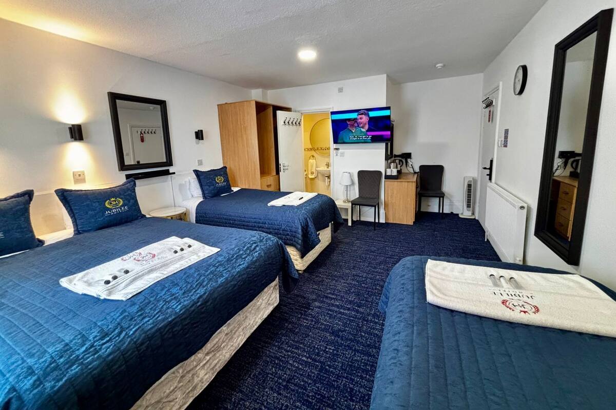 A hotel room with two beds, a TV, a desk, a chair, a mirror, and a clock on the wall.