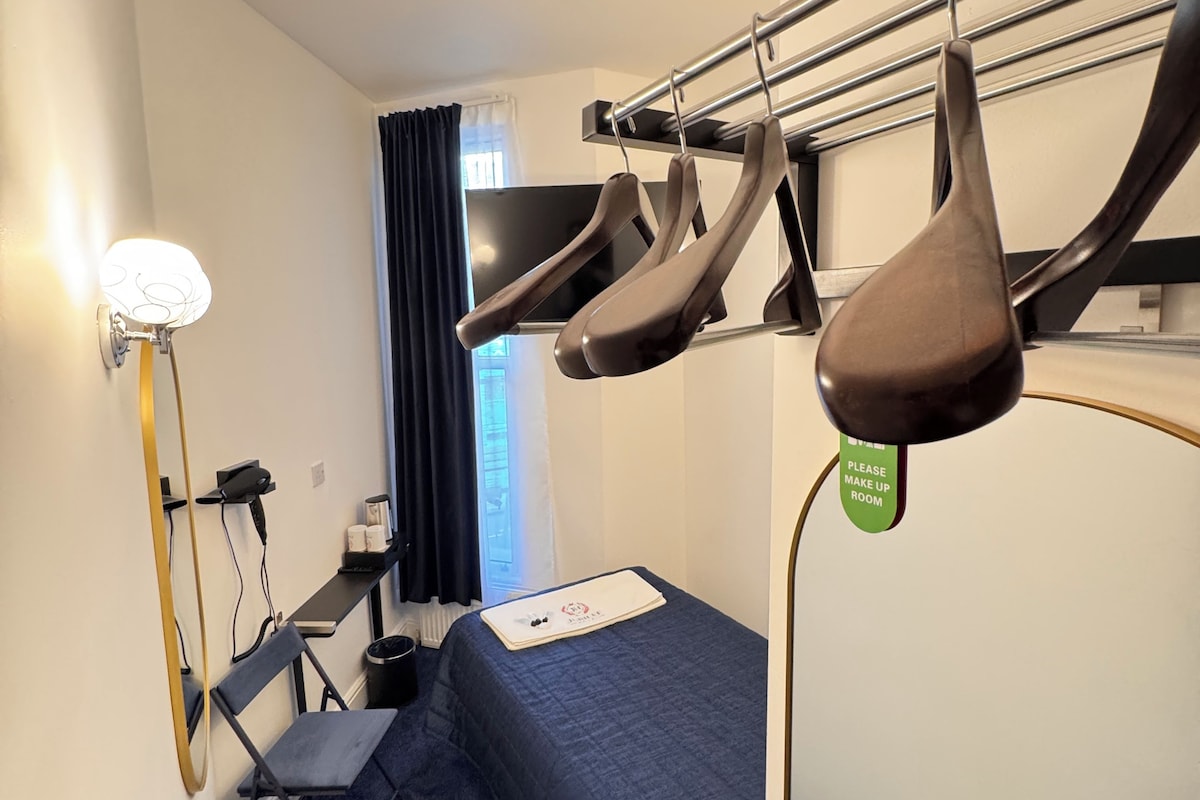 A compact hotel room with a bunk bed, a desk with a chair, a flat-screen TV, and a window with curtains.
