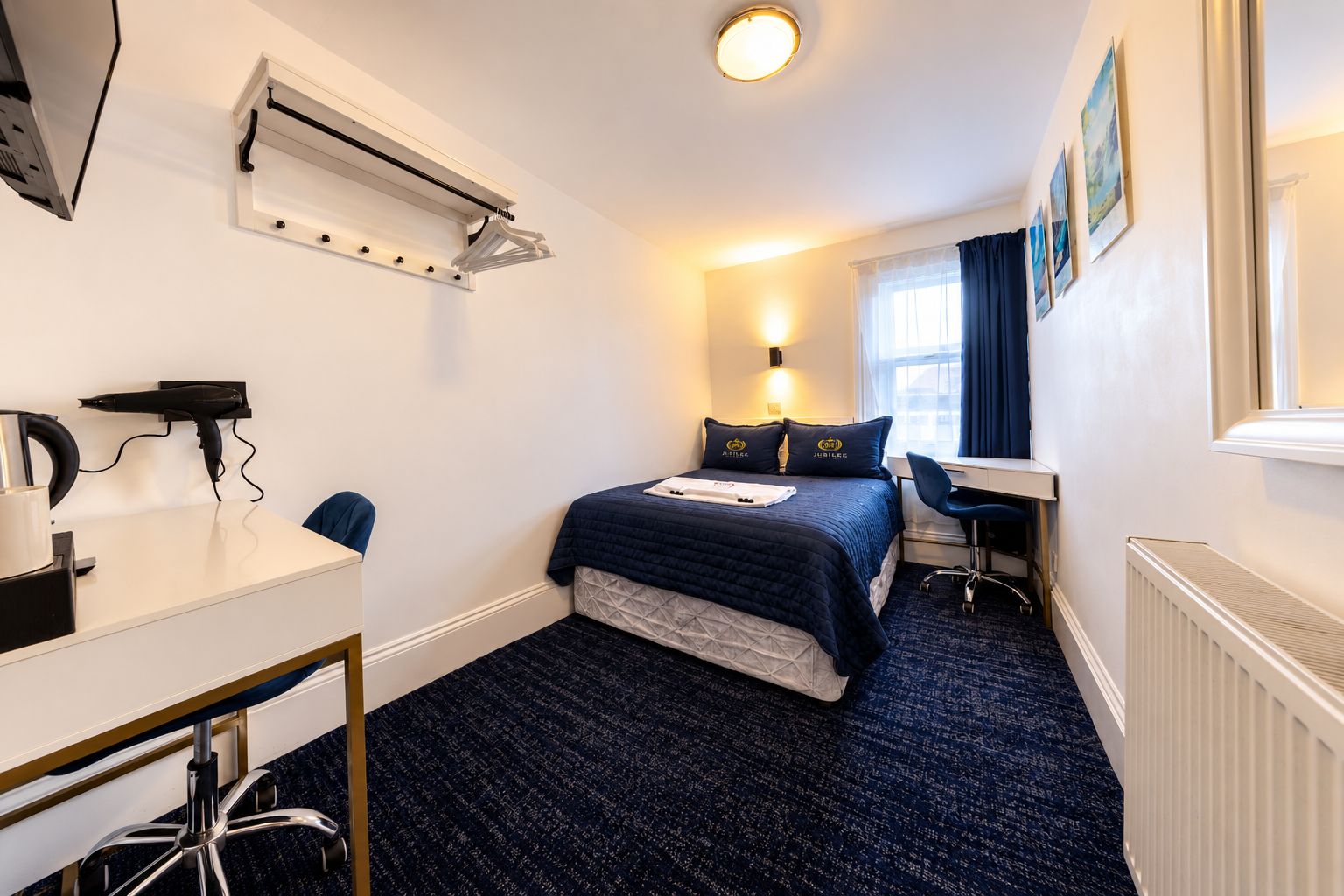 Habitació d'hotel amb llit, escriptori, cadira i un radiador.