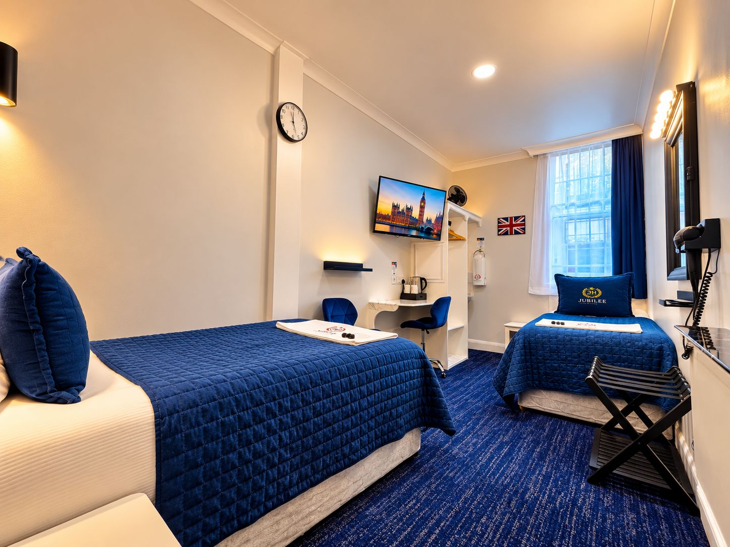 A hotel room with two beds, a desk, a television, a clock, and a window with curtains.