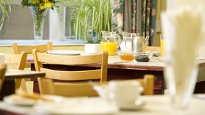 Una mesa de comedor con sillas, un jarrón de flores amarillas y una jarra de jugo de naranja.