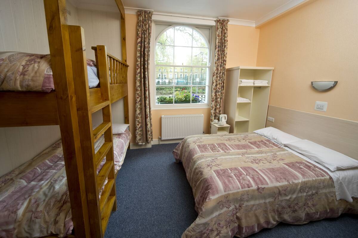 A room with bunk beds, a window with curtains, a radiator, and a shelf with towels.