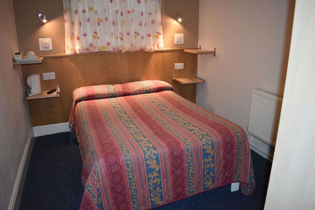 A bedroom with a bed, bedside tables, a radiator, and a window with curtains.