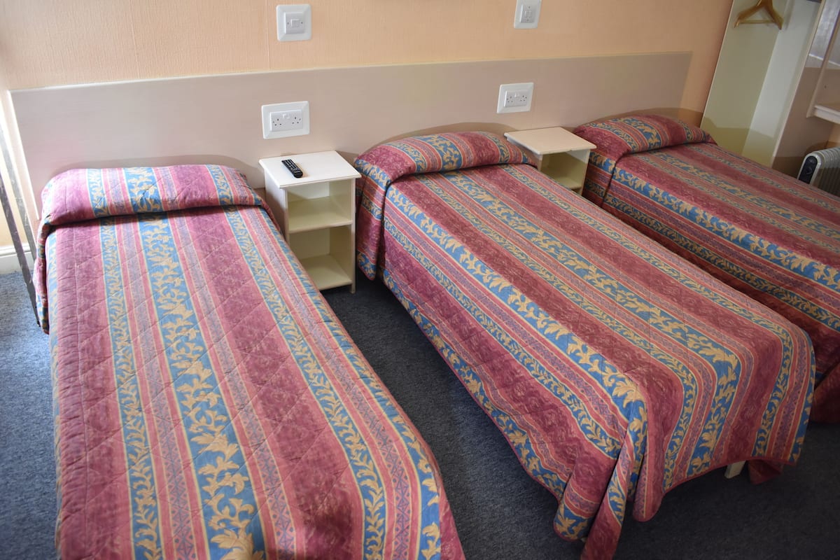 A hotel room with three single beds, each with a patterned bedspread and a bedside table.