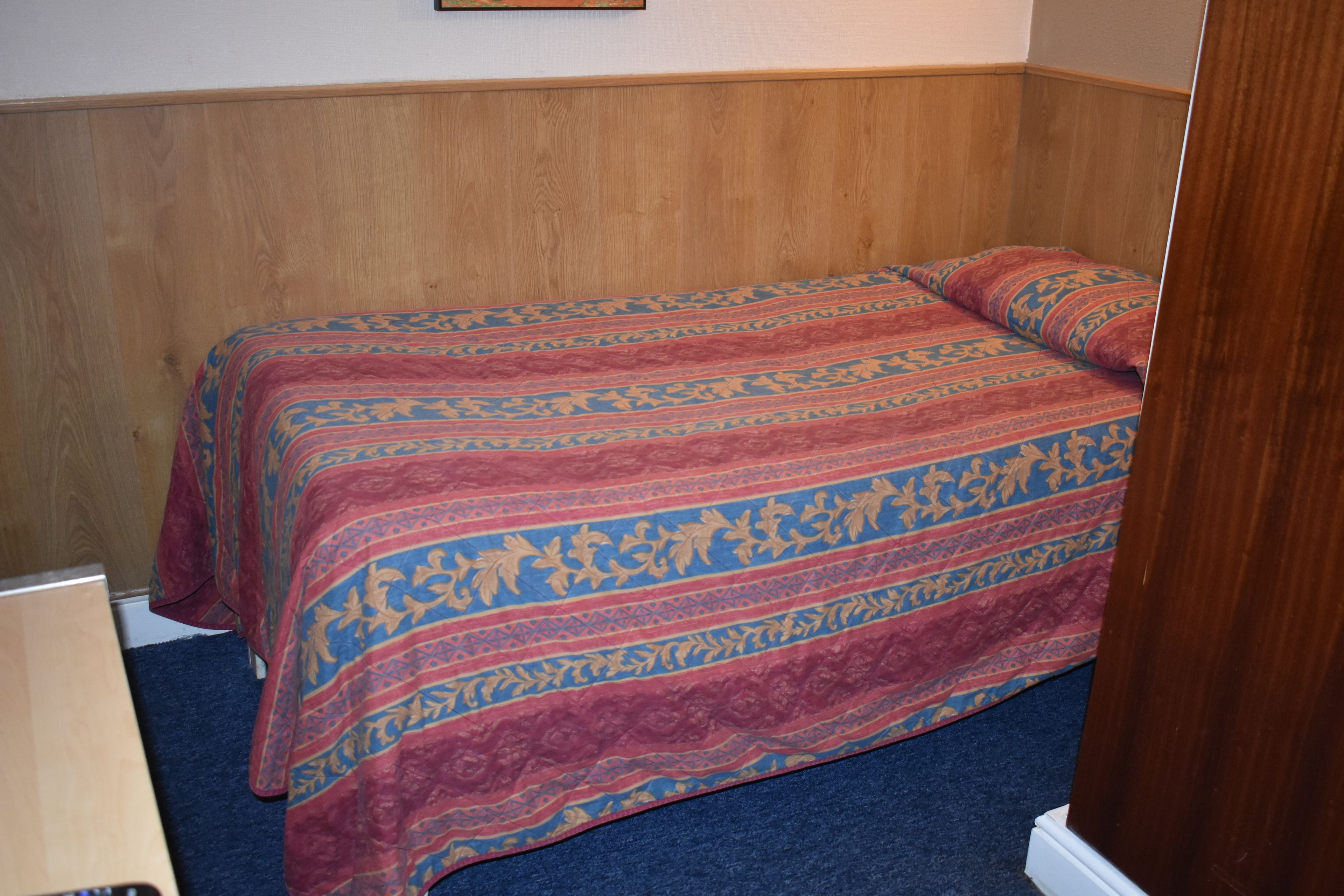 A single bed with a patterned bedspread in a room with wooden paneling on the walls.