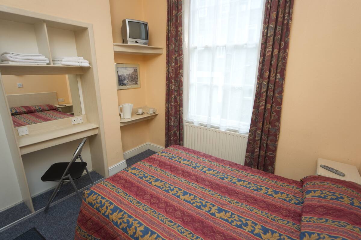 A hotel room with a bunk bed, a desk with a television, a small table with a cup and saucer, and a window with curtains.