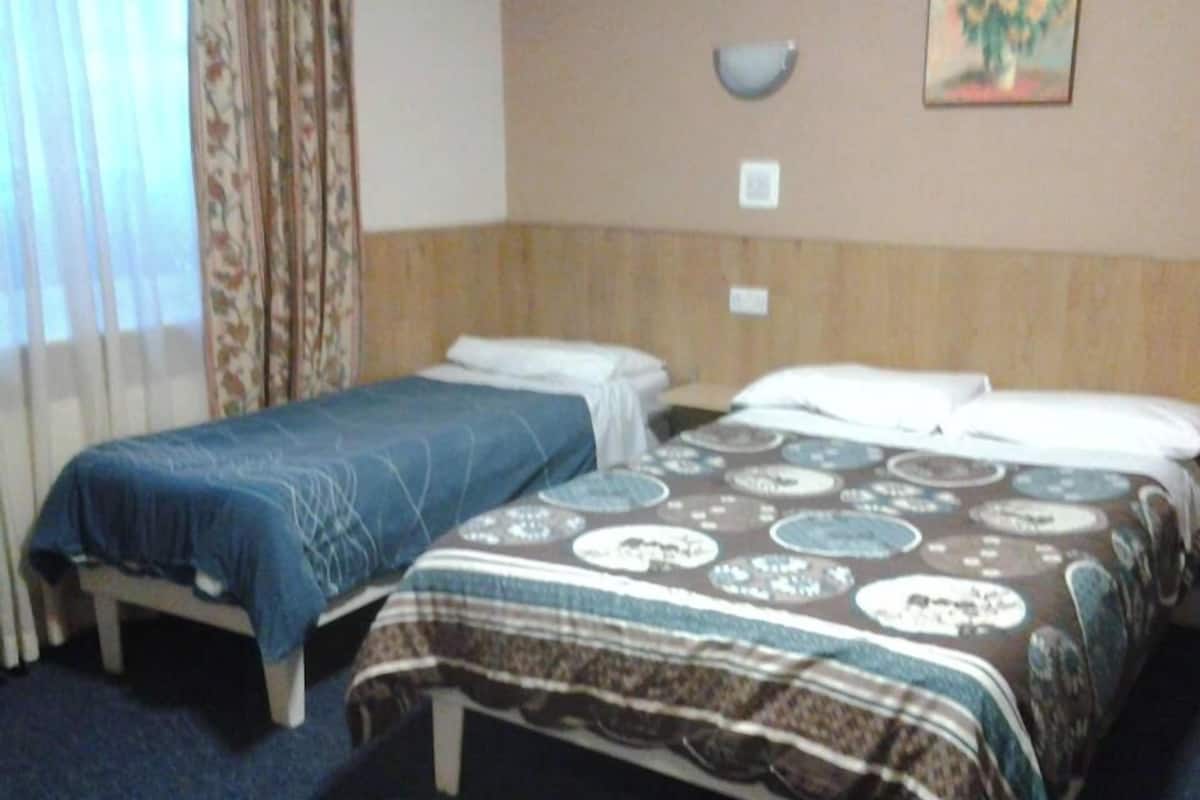 A hotel room with two beds, a wooden headboard, a wall-mounted light, and a painting.