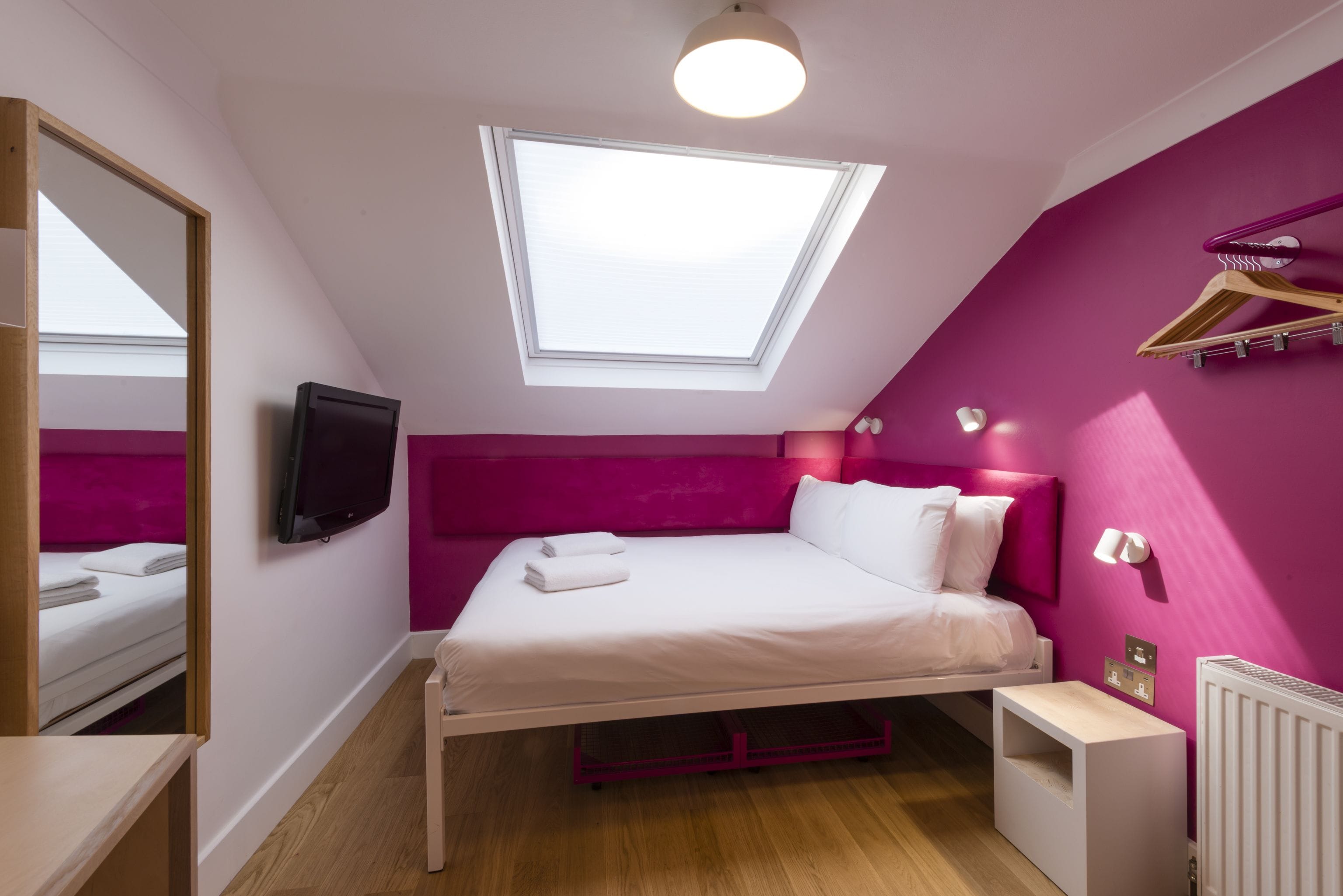 A bedroom with a bed, a TV, a skylight, a radiator, and a wooden dresser.