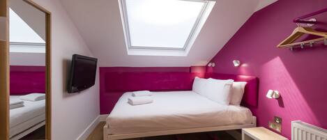 Un dormitorio con cama, televisor, tragaluz, radiador y cómoda de madera.