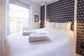 A hotel room with a large bed, two towels, a framed picture on the wall, and a patterned wallpaper. - The California - Kings Cross St Pancras, London (London)