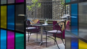 Un espace extérieur aménagé en terrasse, avec un mur en briques, une clôture en métal et une table entourée de chaises.
