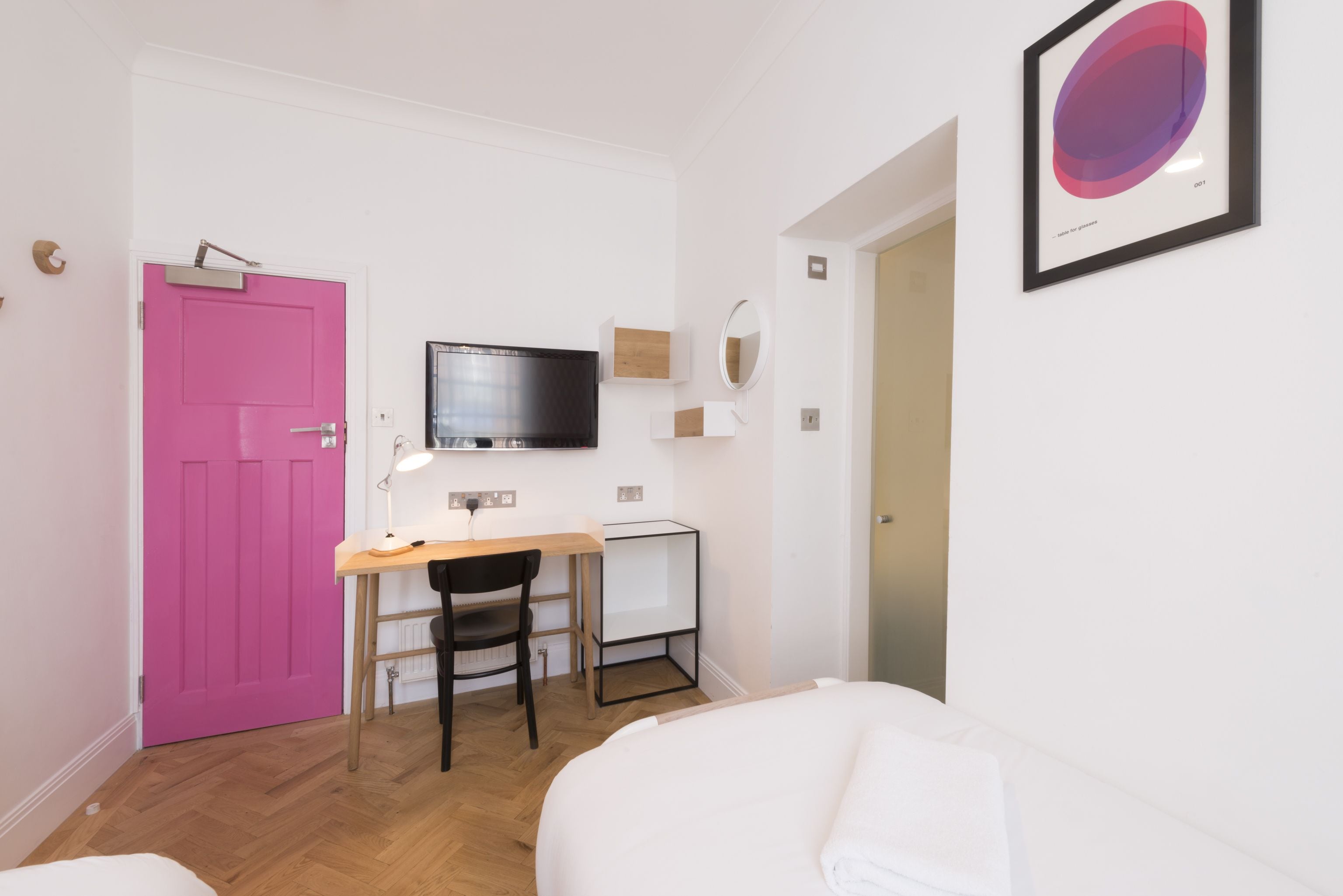 A compact room with a pink door, a desk with a chair, a television, and a bed.