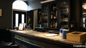Un espace bar doté d’un comptoir en granit, d’étagères remplies de bouteilles et de verres, et d’une boîte en bois posée sur le comptoir.