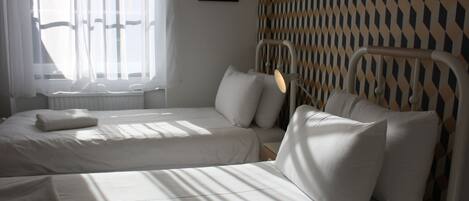 Une chambre d’hôtel avec deux lits, une fenêtre avec des rideaux légers, un mur à motifs et un tableau encadré accroché au mur.