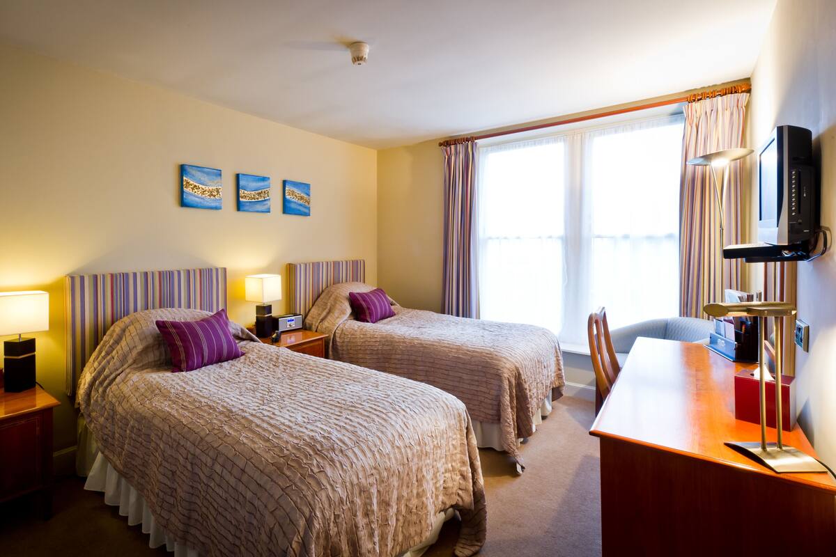 A hotel room with two beds, a desk, a chair, a TV, and a window with curtains.