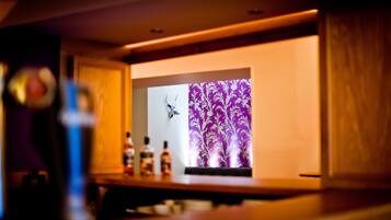 Een bar met een paars patroon als achtergrond, drankflessen en een klein decoratief object op het aanrecht.