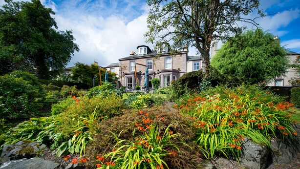 Un grand bâtiment historique, doté d’un jardin à l’avant, où l’on peut admirer une grande variété de plantes et de fleurs.